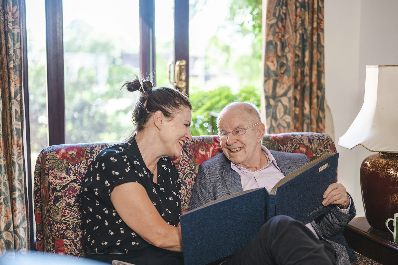 A caregiver and an older man laughing over a photo album at home